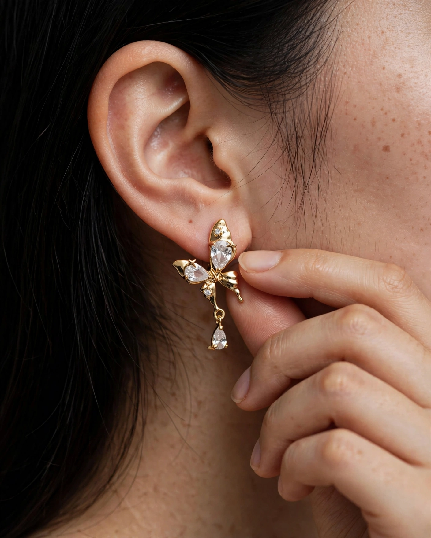 Gold butterfly crystal drop earrings worn on a woman's ear
